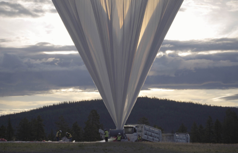 Ein riesiger Ballon, der das Sonnenobservatorium "Sunrise III" trägt. Im Hintergrund sind Wolken und Landschaft zu sehen.