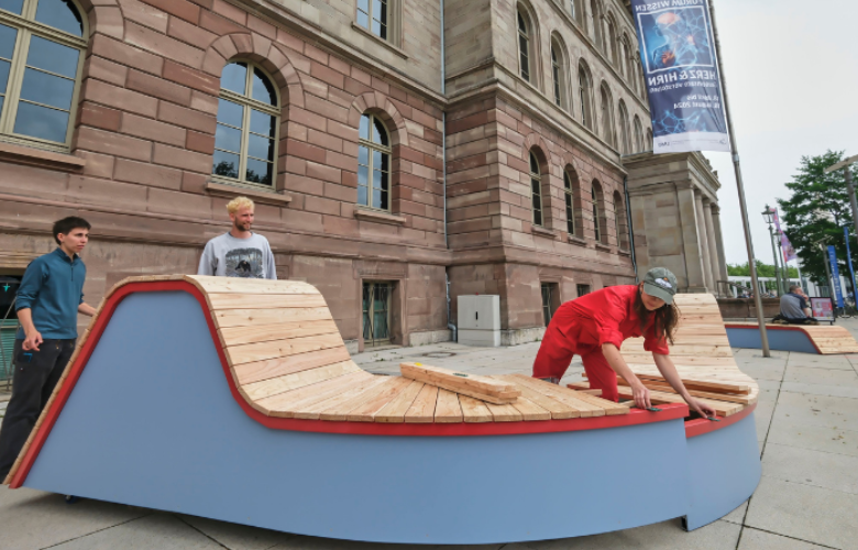 Der Produkt-Designer Jona Wentzler aus Kassel unseren Vorplatz hat geschwungene Sitzgelegenheiten aus Holz auf dem Vorplatz des Forum Wissen gebaut, die zum Verweilen einladen.